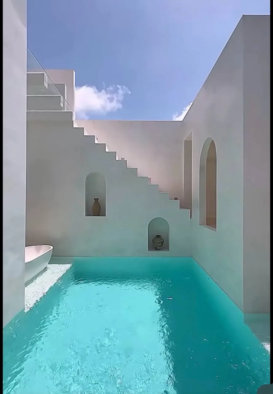 Grey plaster courtyard with standing water and arched niches, then finished white walls, stairs, niches, and pool.