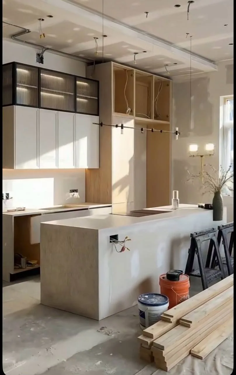 Fluted Island Kitchen with Reeded-Glass Uppers — before — Kitchen island and cabinetry mid-install on bare floor, then finished fluted island, reeded-glass uppers, and stone tops.