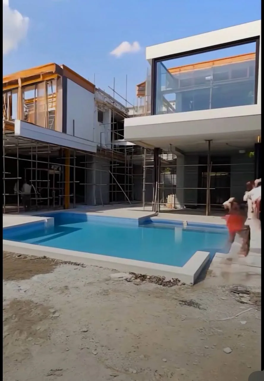 Modern Glass Villa: Pool Courtyard & Landscape — before — Pool courtyard with scaffolding and bare earth, then finished wood-soffit villa with manicured beds and paver walk.