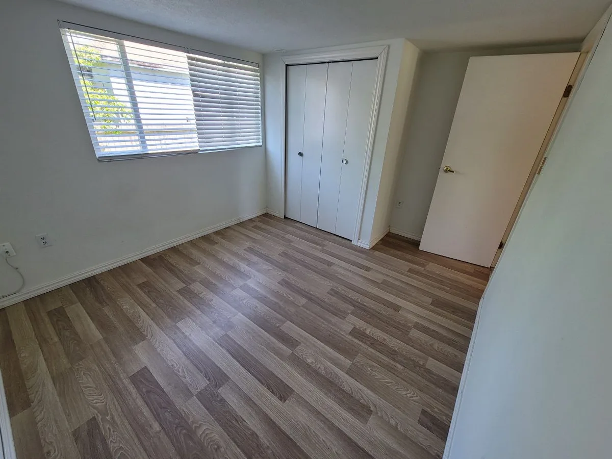 Same light plank floor during wall remediation, then finished bedroom with white closet doors.