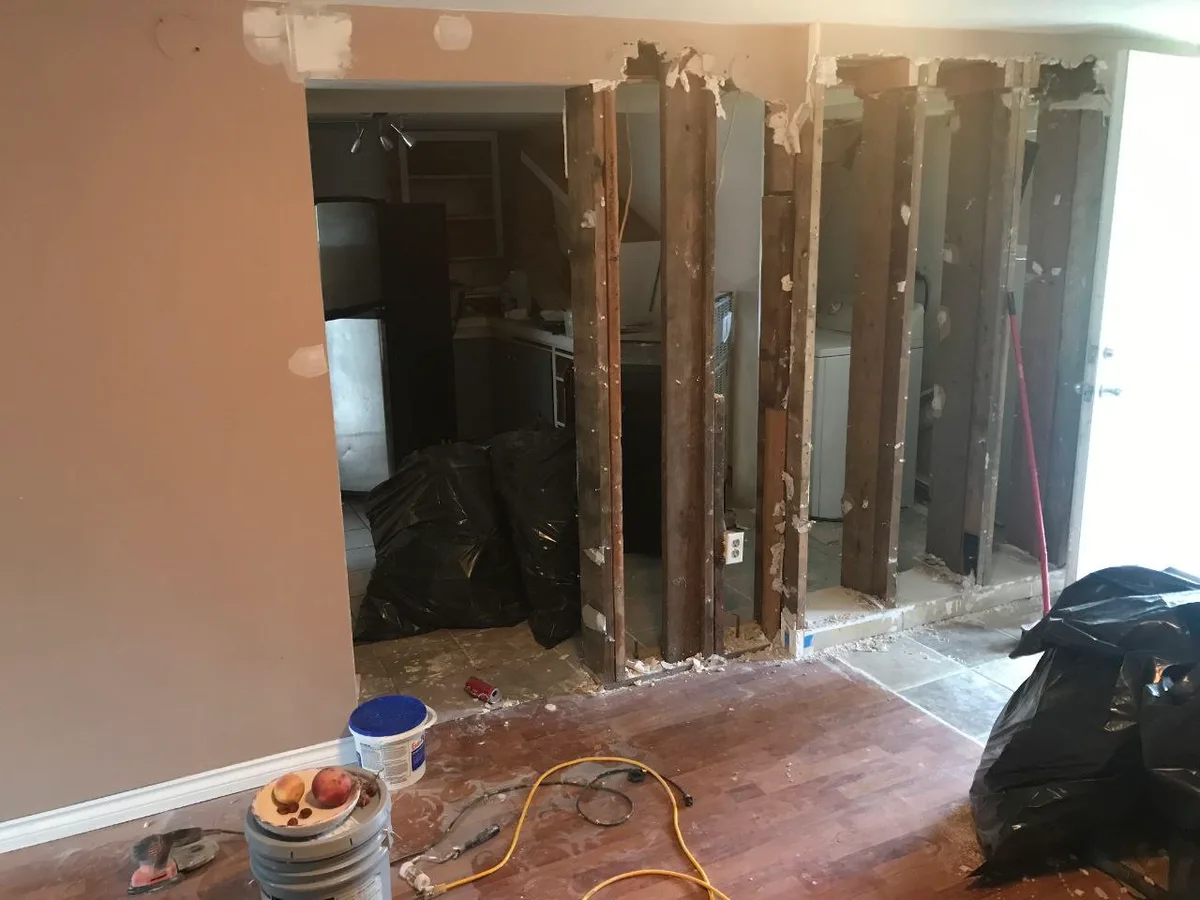 Metro Vancouver Interior: Flooring, Kitchen & Bath — before — Partition opened to kitchen and laundry during demolition, then finished white kitchen with stacked laundry.