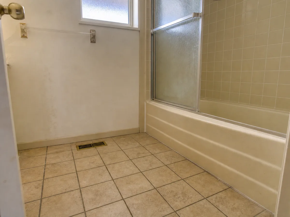 Worn beige tile and tub corner with frosted window before renovation, North Vancouver