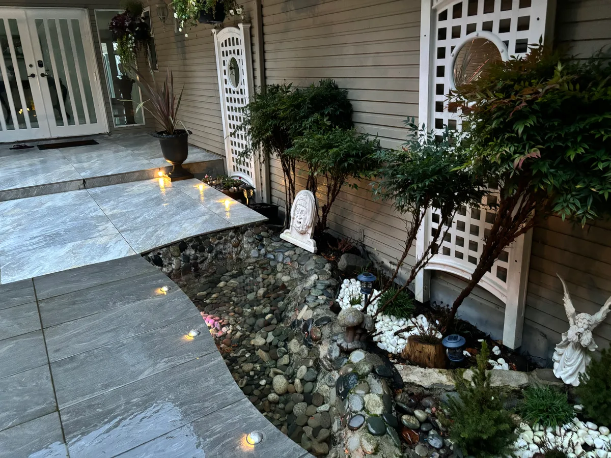Side-of-house rock retaining corridor during construction, then finished lit stone path and planted rock garden along the house wall.