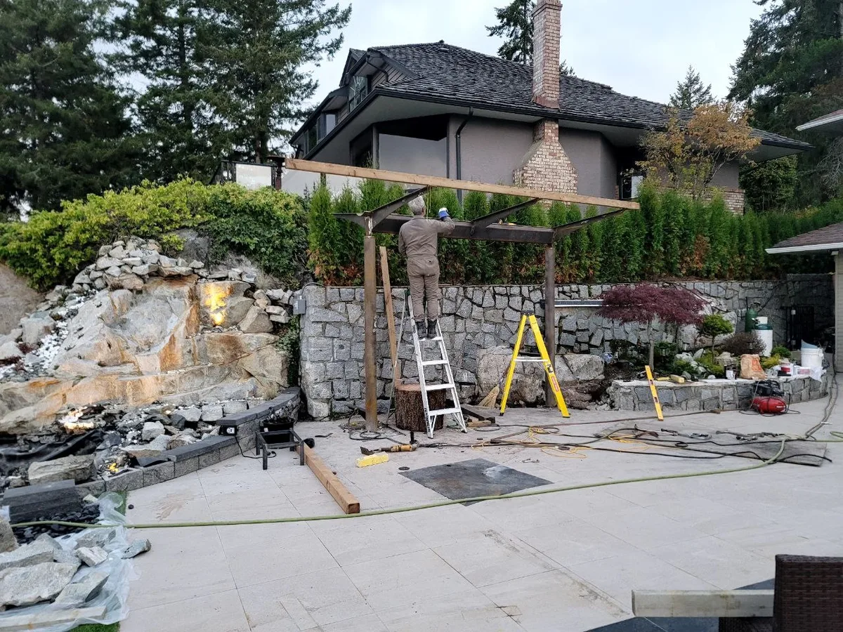West Vancouver Outdoor Kitchen & Glass Canopy — before — Timber framing for the overhead cover, then completed glass-roof canopy over the outdoor kitchen.